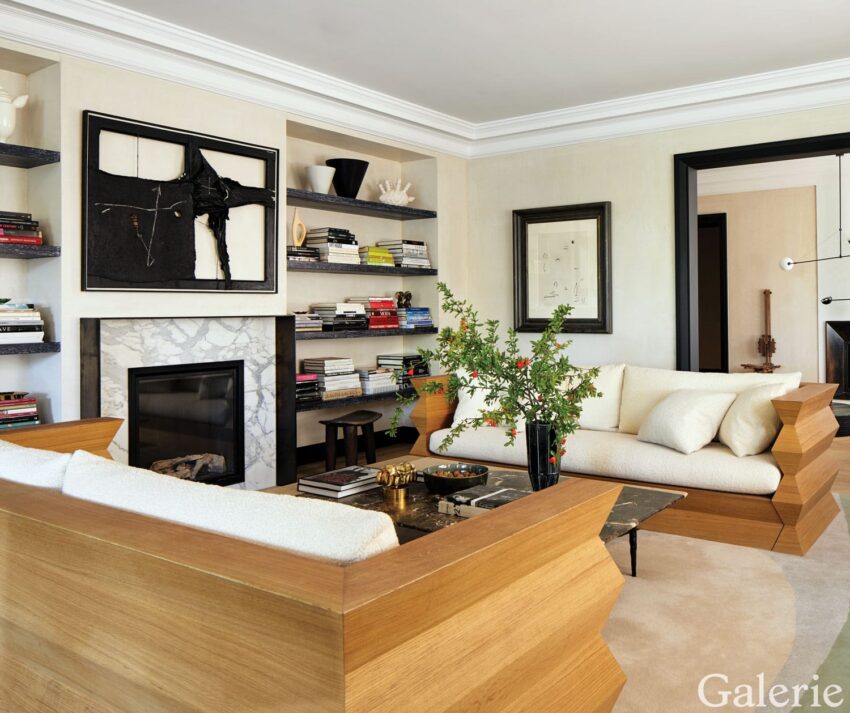 Modern living room with white sofas, wooden accents, bookshelves, wall art, and a marble fireplace surrounded by books.