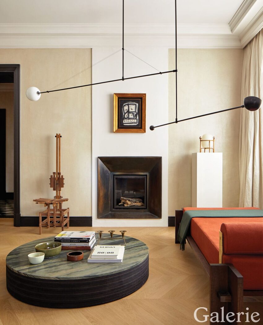 Modern living room with a circular coffee table, abstract wall art, minimalist fireplace, and contemporary lighting fixture.