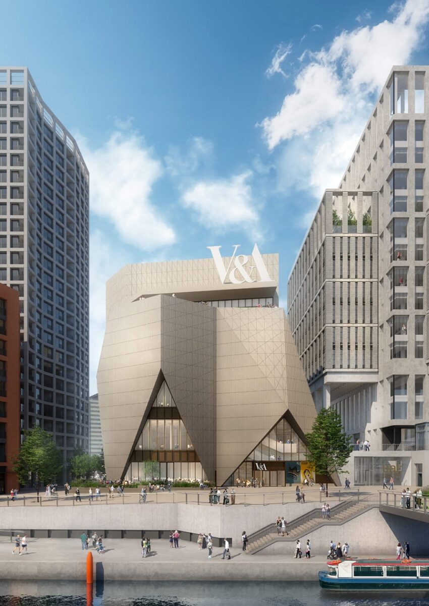 Modern V&A Museum building with geometric design surrounded by skyscrapers, viewed from a riverside walkway.