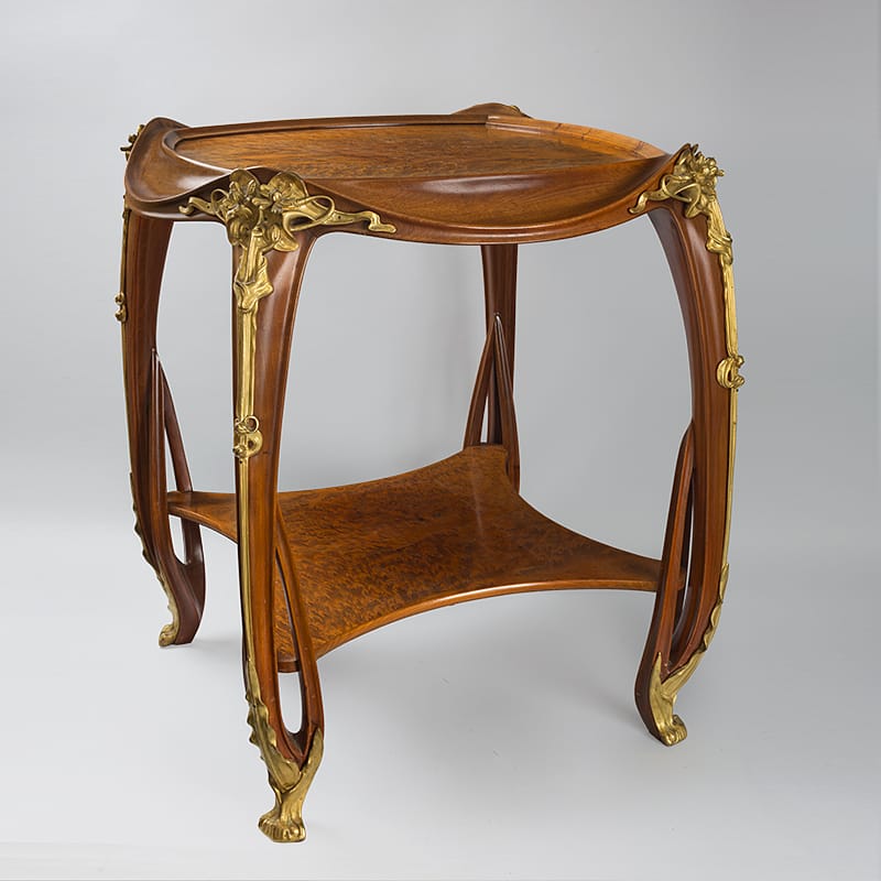 Art Nouveau wooden table with curved legs and ornate floral brass accents.