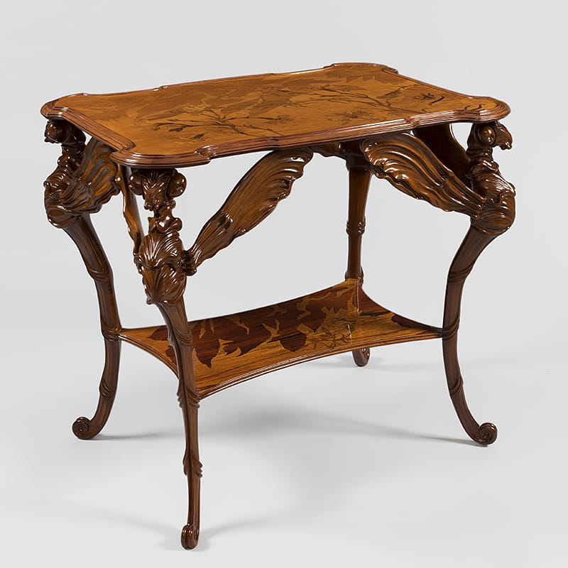 Antique wooden table with intricate carvings and decorative details on legs and edges, displaying leaves and vine motifs.