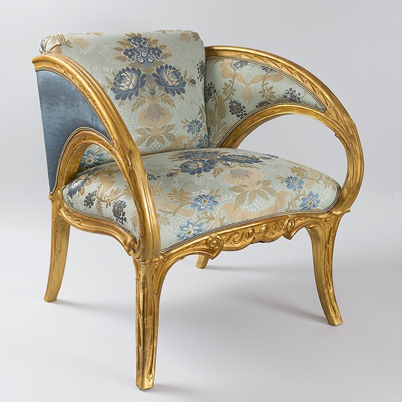 Vintage armchair with ornate gold frame and floral upholstery on a light background.
