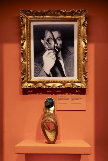 Framed abstract portrait above a shelf displaying a unique high-heeled shoe sculpture in a museum setting.