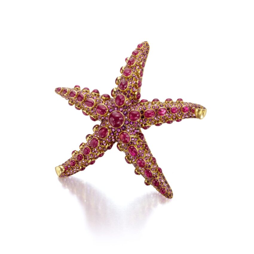 Starfish-shaped jewel decorated with red gemstones and gold accents on a white background.