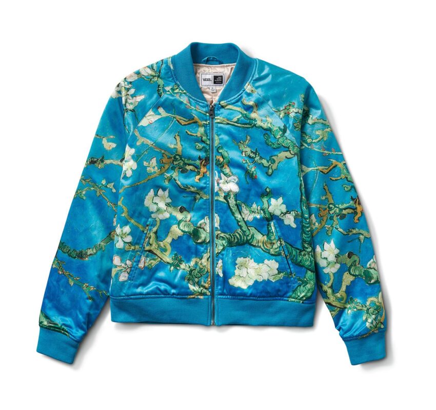 Blue bomber jacket with a floral design featuring branches and white blossoms against a vibrant background.
