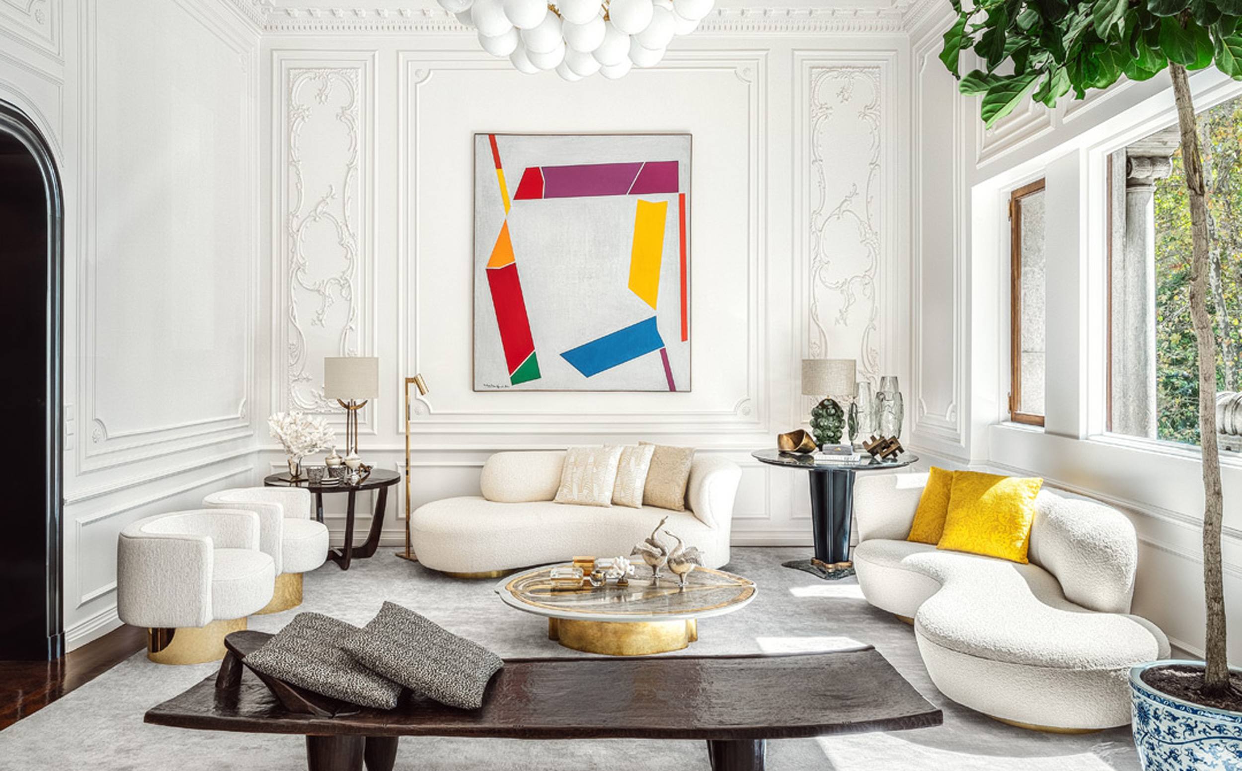 Modern living room with abstract artwork, white furniture, and a large window providing natural light.