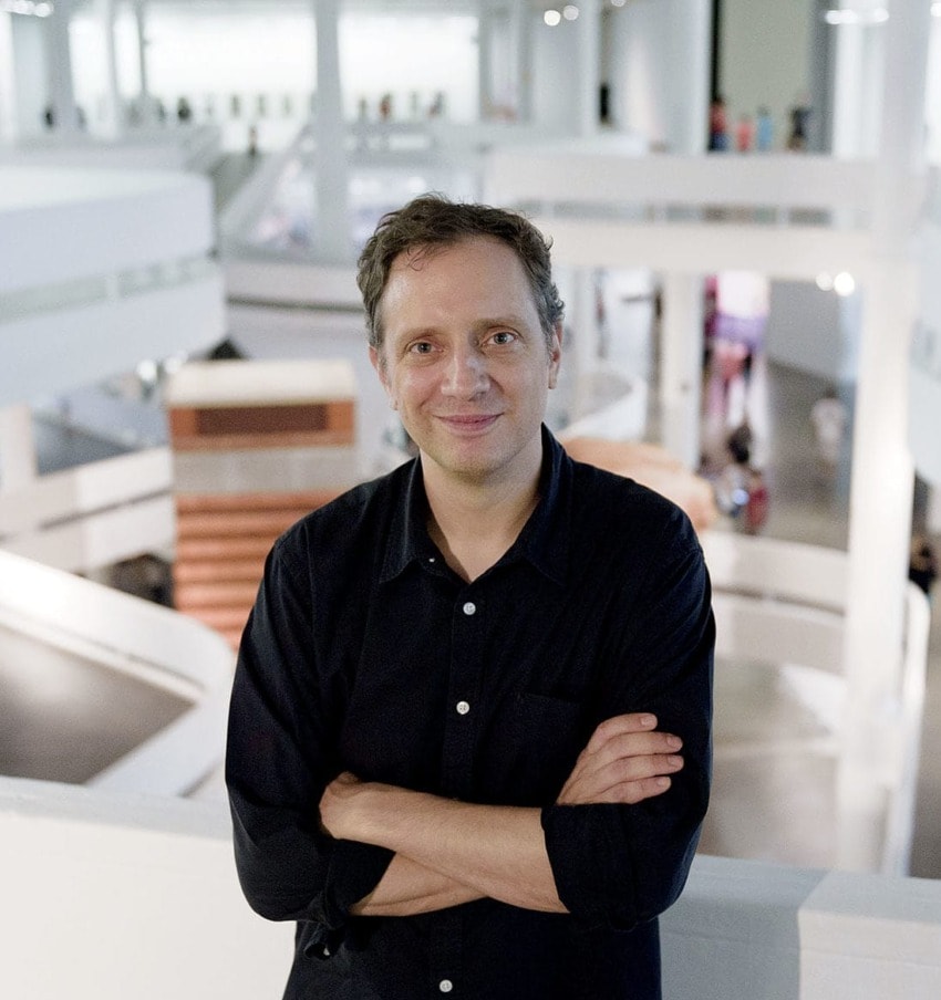 Man smiling in a modern art museum with white architectural elements in the background.