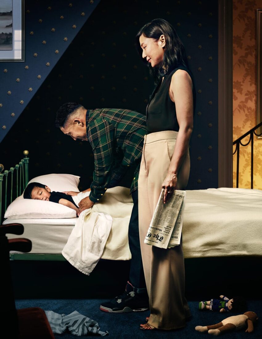 Child sleeping in bed while adults tuck them in, with toys on the floor, creating a warm and caring bedtime scene.