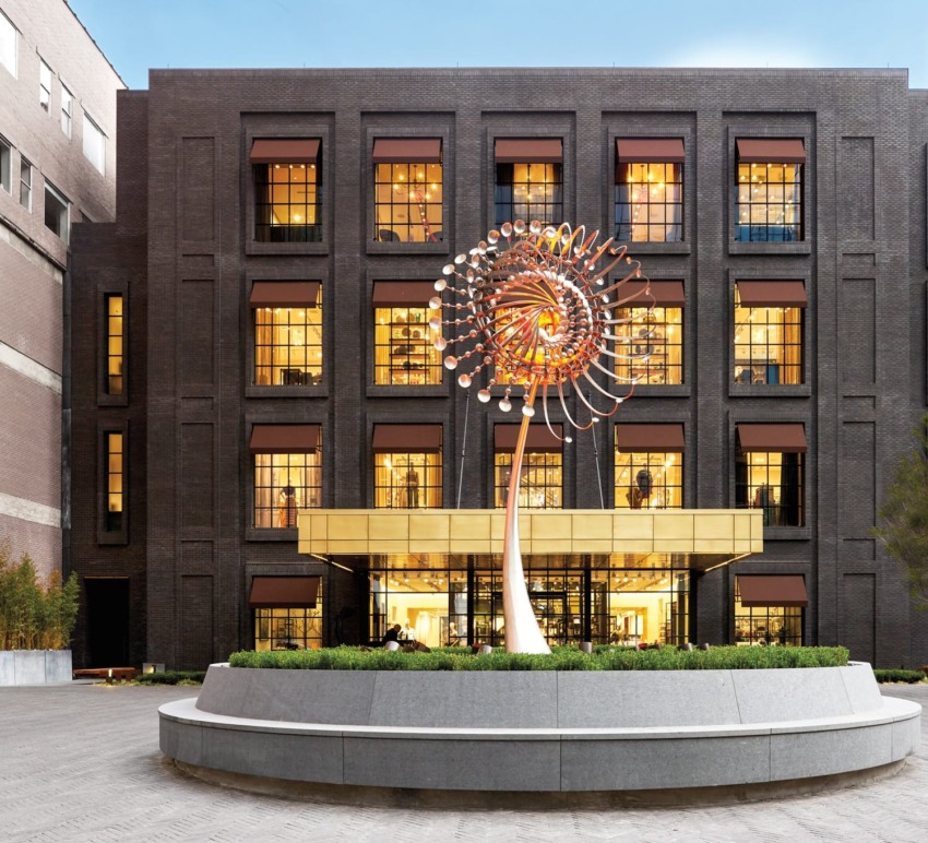 Modern building with a large, colorful spiral sculpture in front, surrounded by greenery and clear sky above.