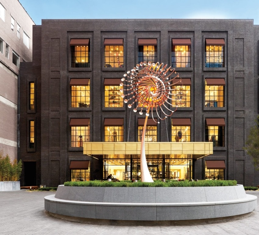 Modern building with a large, colorful spiral sculpture in front, surrounded by greenery and clear sky above.