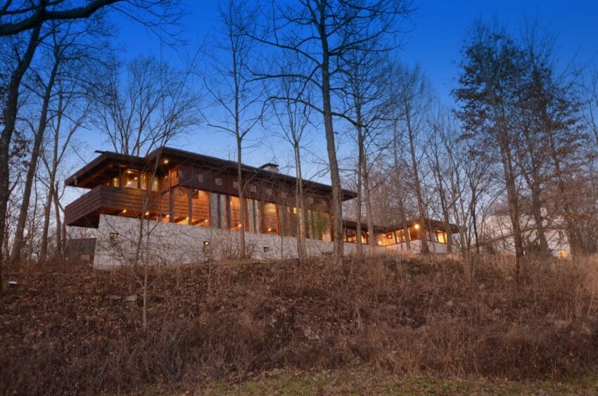 Modern house surrounded by bare trees in a forest during twilight with a clear blue sky.