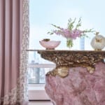 Elegant room with a pink rose quartz table, floral centerpiece, and delicate drapes overlooking a cityscape.