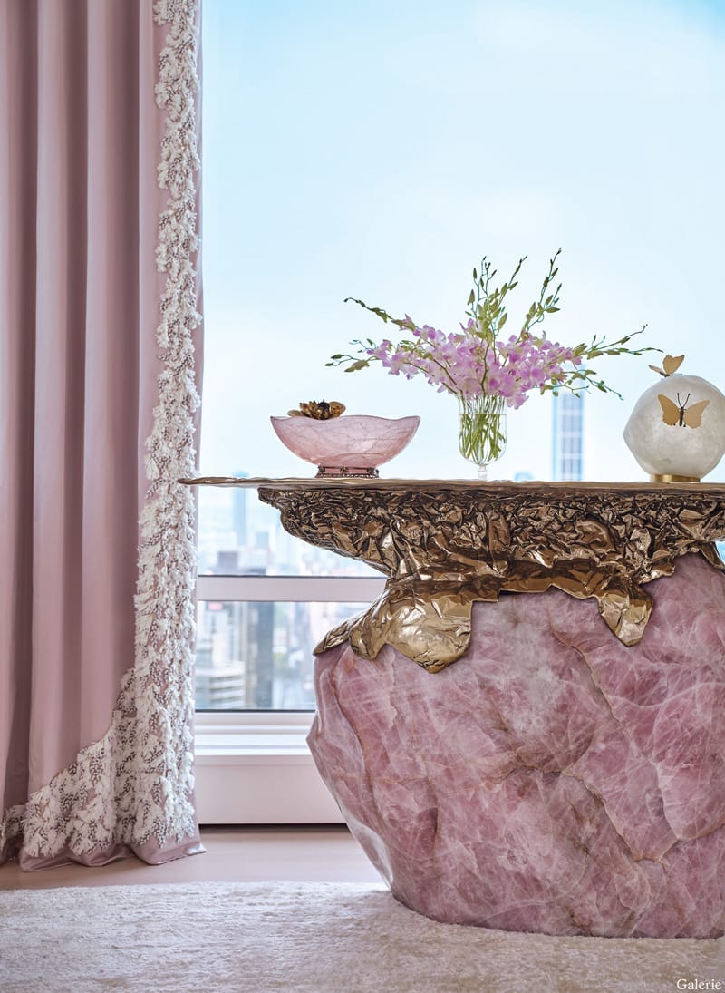 Elegant room with a pink rose quartz table, floral centerpiece, and delicate drapes overlooking a cityscape.
