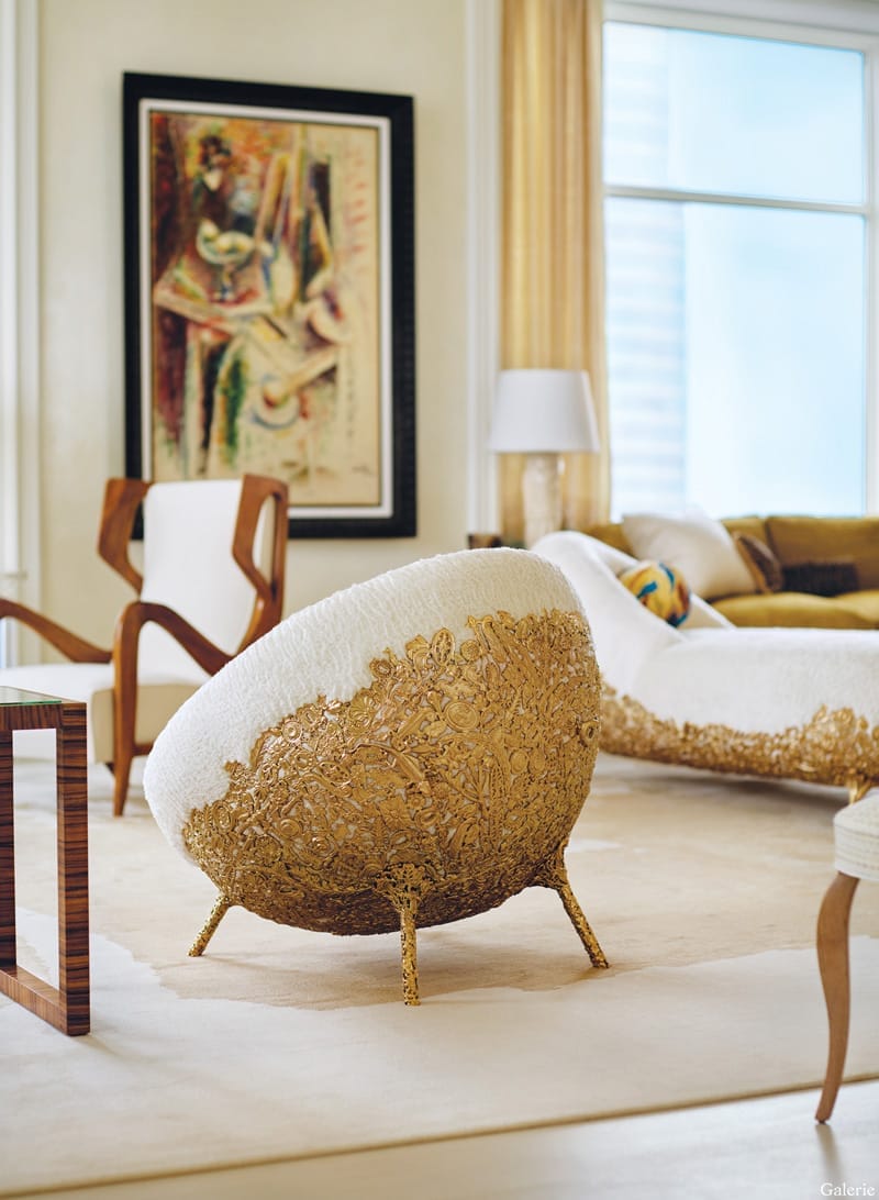Luxurious living room with a uniquely designed gold and white chair, modern art on the wall, and elegant decor elements.