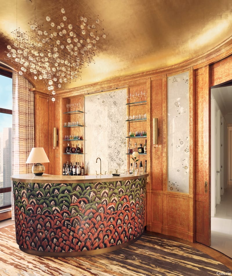 Luxurious home bar with curved counter, elegant glass shelving, gold ceiling, chandelier, and large windows with city view.