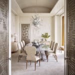Elegant dining room with a glass table, patterned chairs, decorative chandelier, and textured walls.