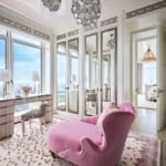 Luxurious room with pink chaise lounge, mirrored wardrobe, large windows, and elegant chandeliers.
