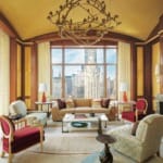 Elegant living room with large windows, modern furniture, unique chandelier, and city skyline view in the background.