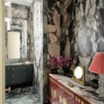 Luxurious bathroom with intricate marble walls, elegant furnishings, red dresser, and decorative lighting.