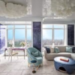 Luxurious modern living room with blue and white accents, featuring a large window overlooking a cityscape.