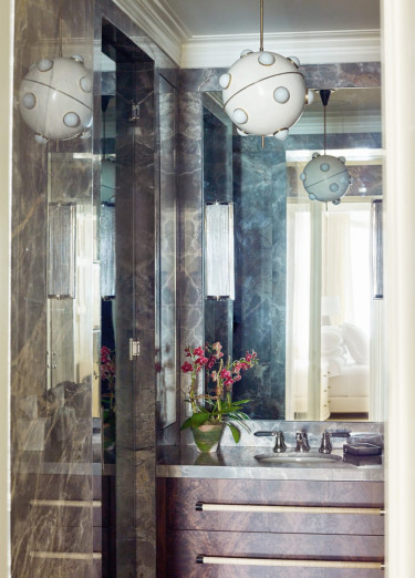 Elegant bathroom with marble walls, modern pendant lights, a sleek vanity, and a small vase with flowers.
