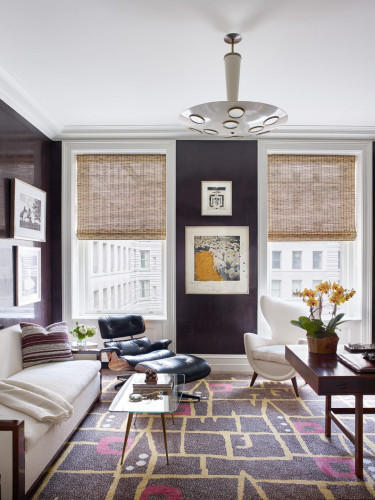 Modern living room with white sofa, armchairs, abstract rug, wall art, and large windows letting in natural light.