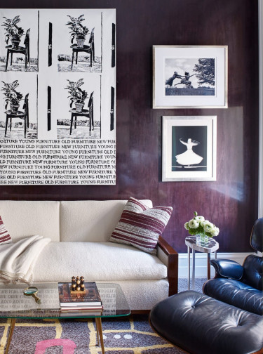 Modern living room with patterned artwork, cream sofa with striped pillows, and black lounge chair on a colorful rug.