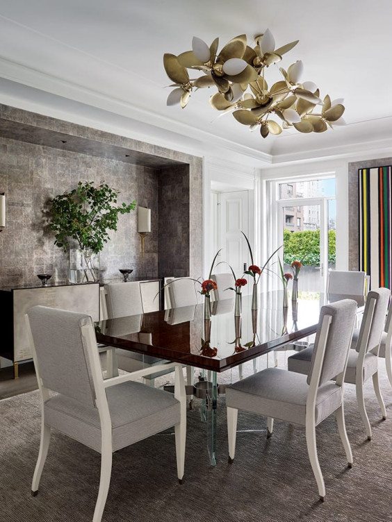 Elegant dining room with a modern chandelier, glass-topped table, white chairs, and decorative vases with flowers.