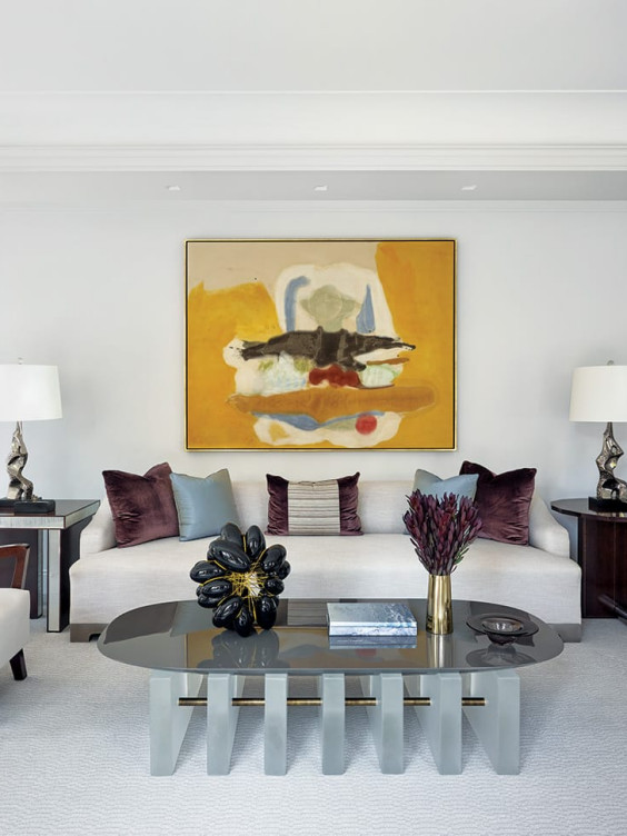 Modern living room with abstract painting, cream sofa, dark coffee table, decorative pillows, lamps, and stylish accents.