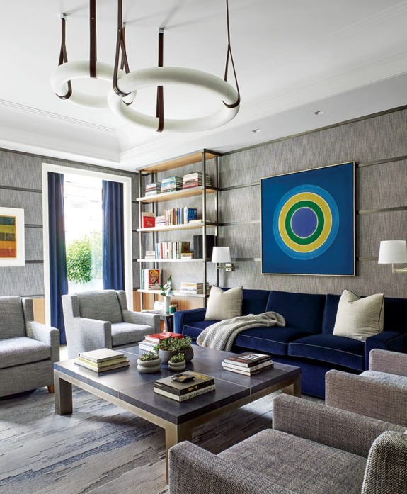 Modern living room with gray walls, navy sofa, round chandeliers, bookshelves, and abstract art.