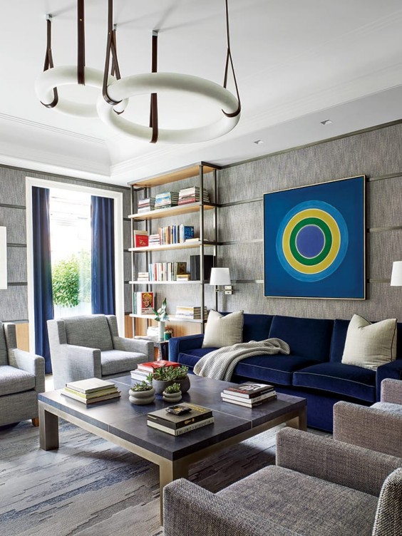 Modern living room with gray walls, navy sofa, round chandeliers, bookshelves, and abstract art.