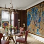 Colorful dining room with abstract painting, red-striped chairs, round glass table, and eclectic decorations.