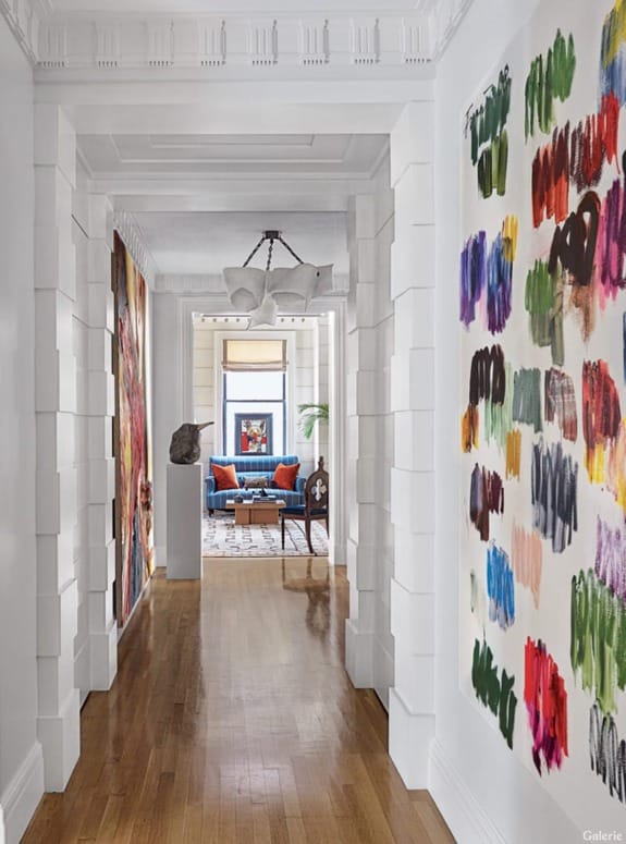 Bright hallway with colorful abstract art, leading to a room with blue chairs and natural light.