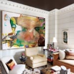 Modern living room with abstract colorful painting, beige armchairs, and eclectic decor including a small sculpture on the table.