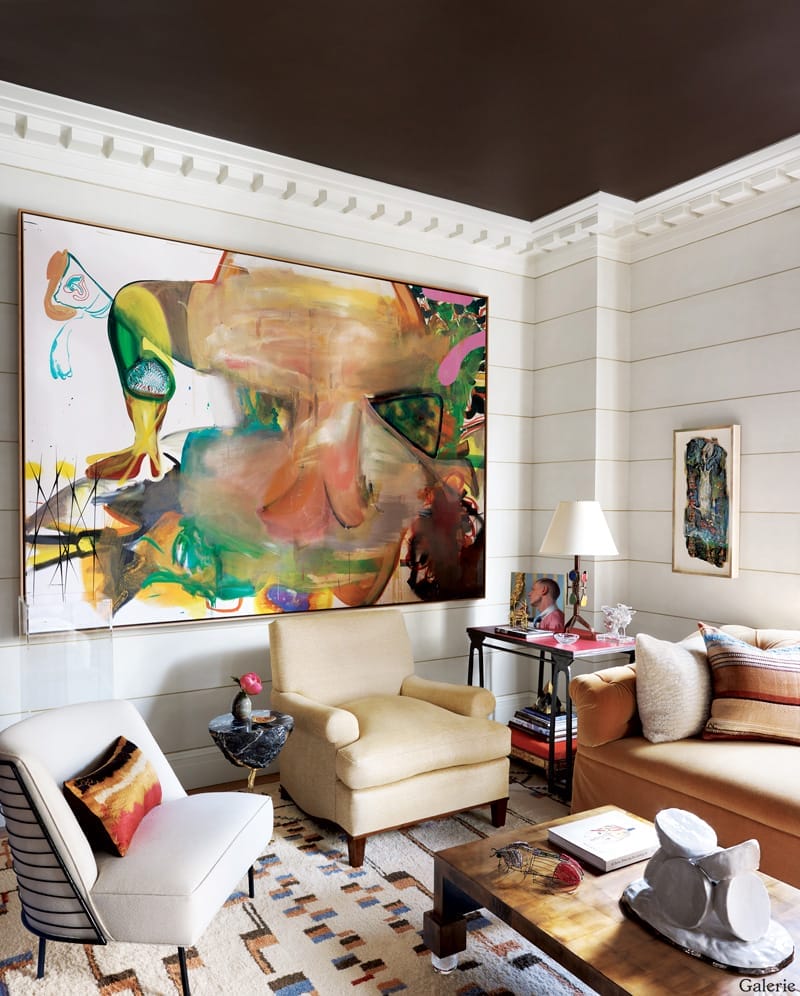 Modern living room with abstract colorful painting, beige armchairs, and eclectic decor including a small sculpture on the table.