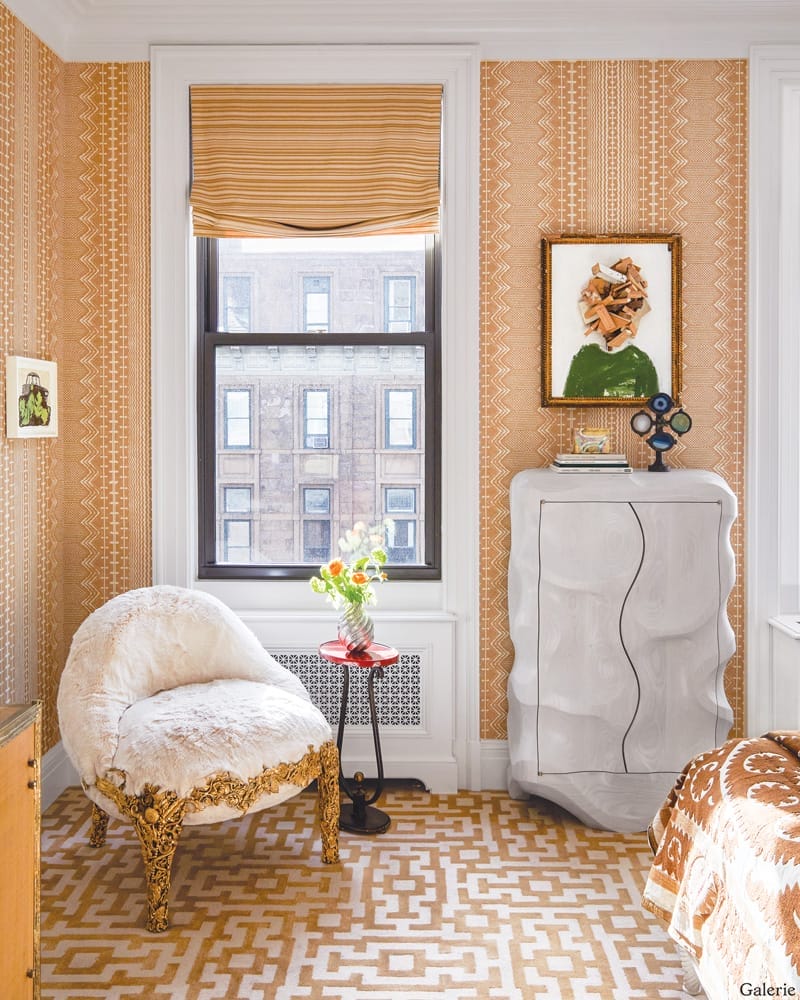 Cozy room with patterned wallpaper, elegant chair, small table with flowers, abstract art, and a wavy dresser.