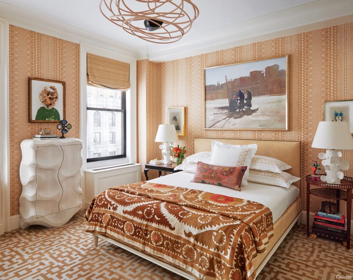 Bedroom with orange patterned wallpaper, modern art, and a geometric ceiling light fixture above a neatly made bed.