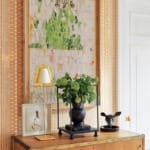 decorative sideboard with plants, a lamp, framed art, and a geometric wallpaper pattern in a well-lit room