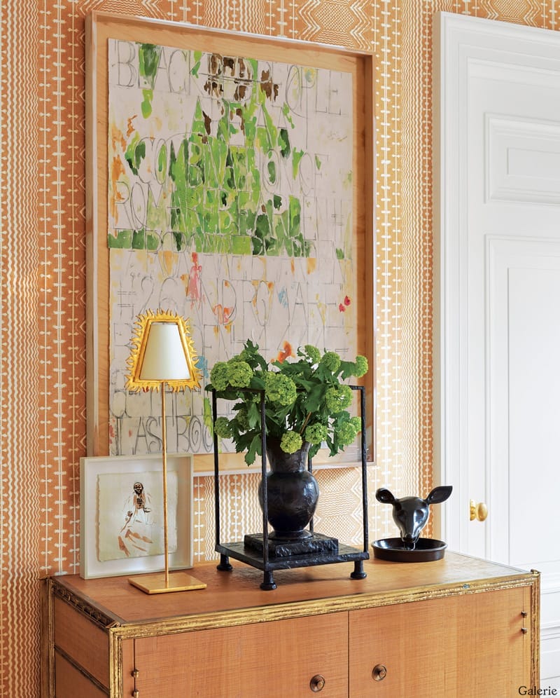 decorative sideboard with plants, a lamp, framed art, and a geometric wallpaper pattern in a well-lit room