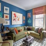 Eclectic living room with vibrant blue walls, green sofa, patterned rug, and diverse artwork displays.