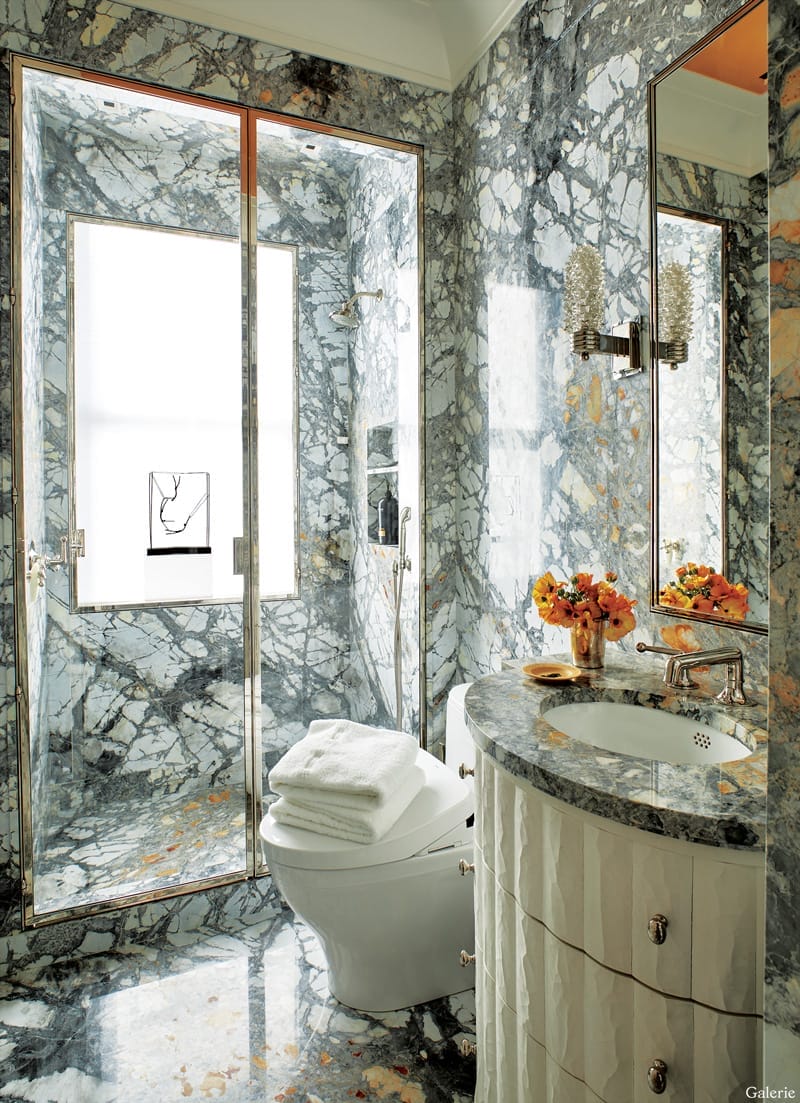 Elegant marble bathroom with a glass shower, modern fixtures, a vase with flowers, and neatly folded white towels on the toilet.