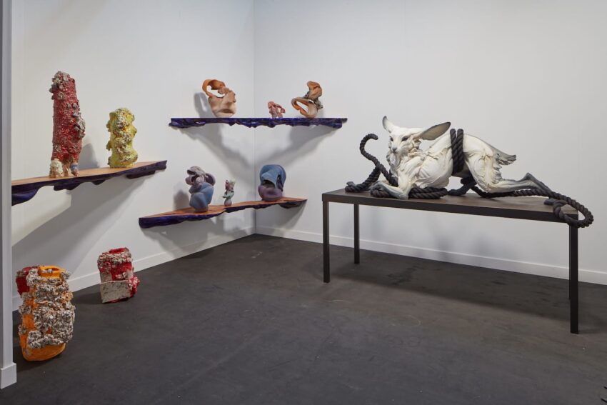 Art gallery exhibit with abstract sculptures on shelves and a table, featuring varied textures and colors in a modern setting.