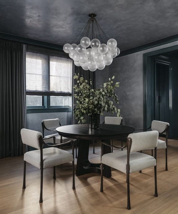 Modern dining room with a round table, four chairs, a large plant centerpiece, and a decorative bubble chandelier.