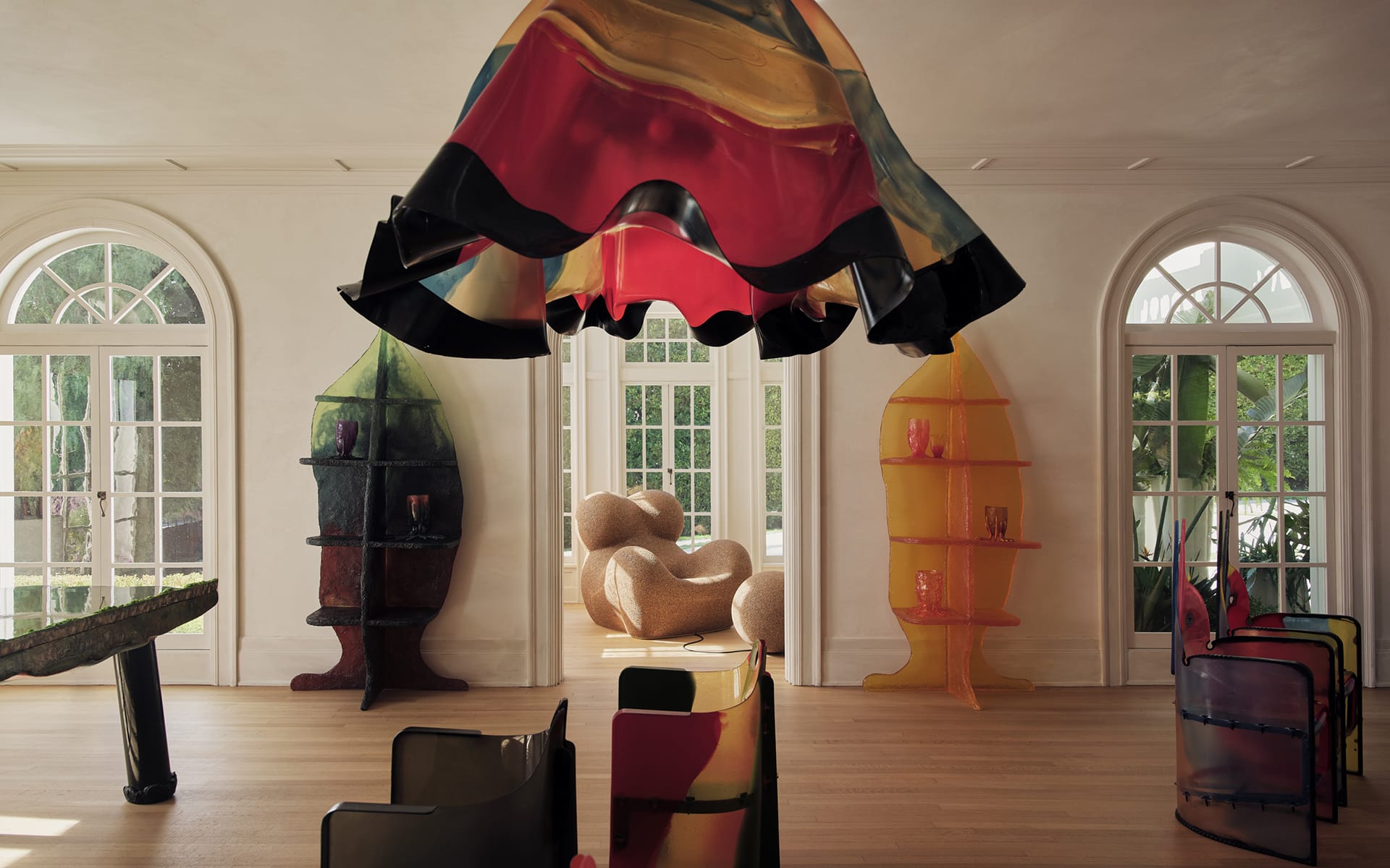 Modern art installation in a bright room with colorful abstract sculptures and natural light streaming through large windows.
