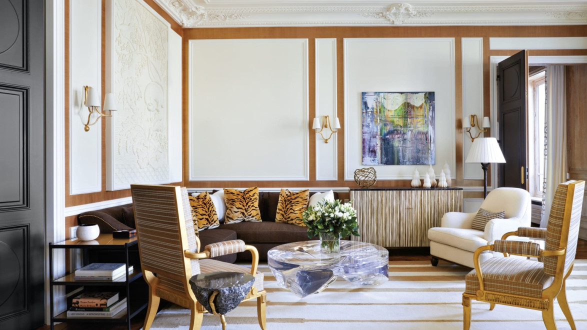 Elegant living room with ornate walls, modern art, striped rug, and mixed seating including armchairs and a stone table.