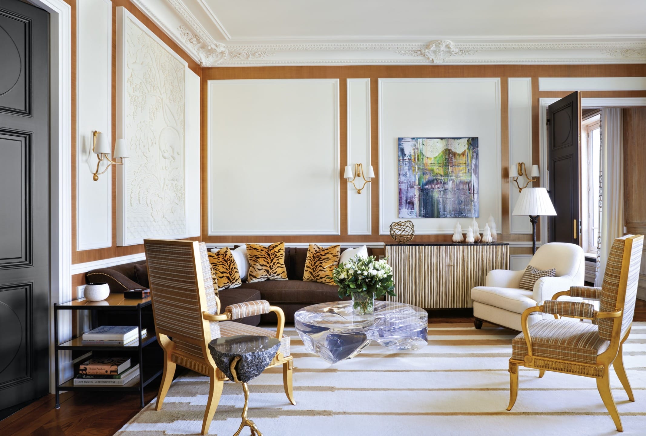 Elegant living room with ornate walls, modern art, striped rug, and mixed seating including armchairs and a stone table.