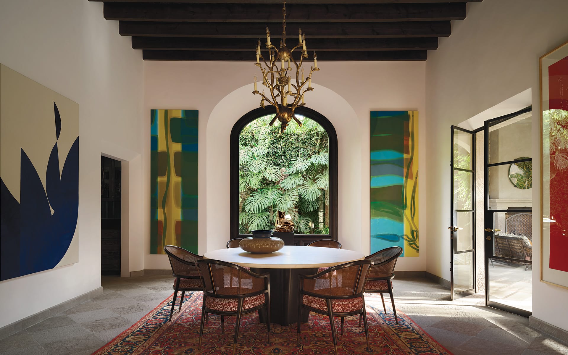 Elegant dining room with modern art, large arched window, and a chandelier above a round table on a decorative rug.
