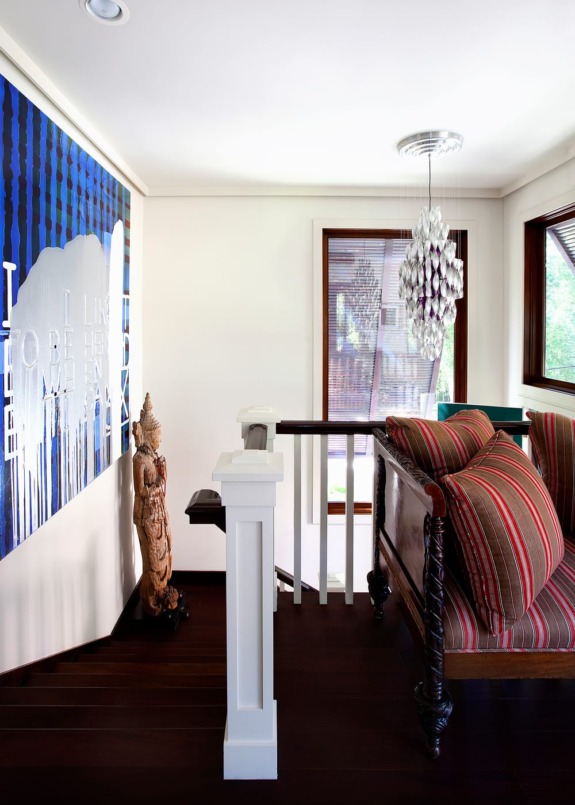 Cozy hallway with striped couch, modern artwork, staircase, wooden statue, and hanging light fixture.