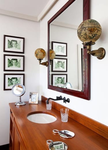 Bathroom vanity with wooden countertop, large mirror, globe-shaped light, and framed photos on the wall.
