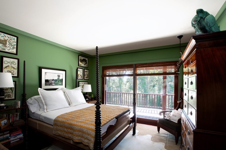 Green-themed bedroom with a four-poster bed, large window, wooden dresser, and various artworks on the walls.